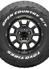 A black Toyo Tires Open Country R/T off-road tire mounted on a dark metallic multi-spoke wheel, shown against a plain white background.
