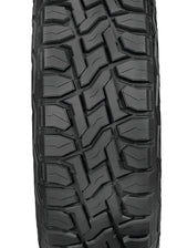 A single black all-terrain tire with a deep, aggressive tread pattern, shown from a front-facing perspective on a solid white background.